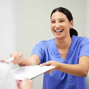 Woman in blue scrubs handing forms on clipboard to patient
