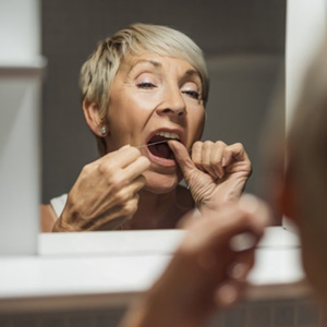 Woman flossing her teeth in bathroom mirror 